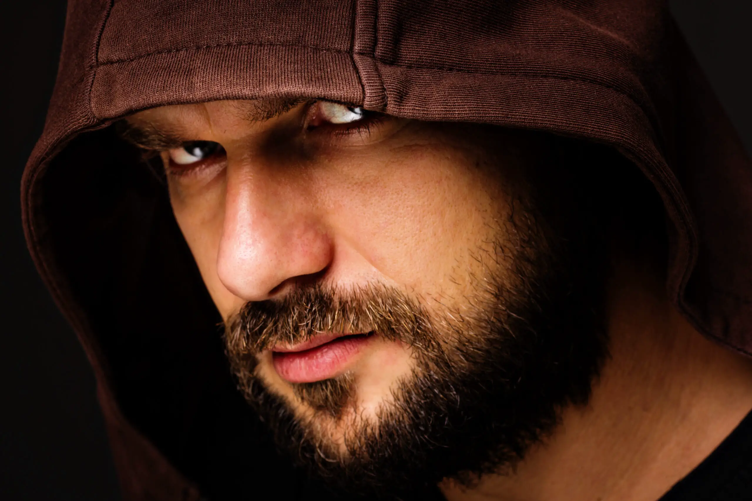 threatening man with beard wearing a hood against gray background
